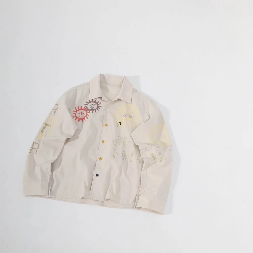 Beige long-sleeve button-up shirt with embroidered smiling suns, bicycles, arrows, and dot patterns
